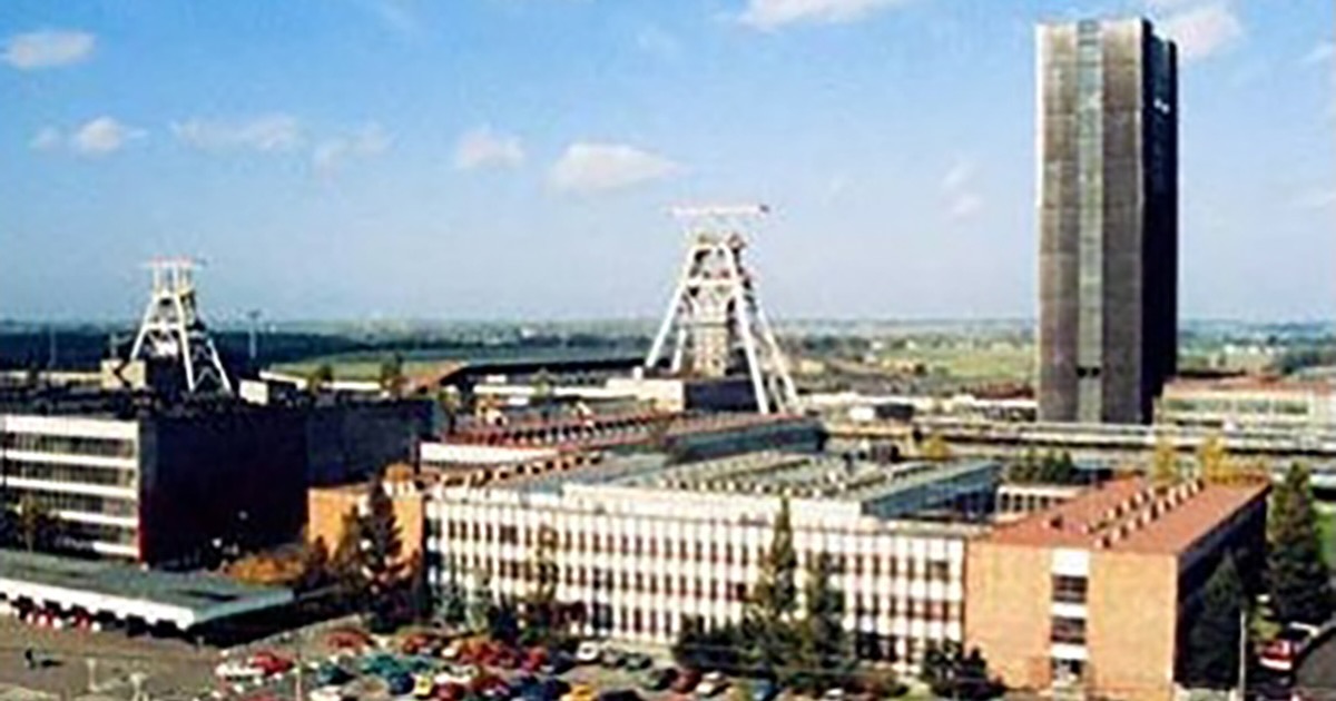 Office and industrial buildings of Jastrzębie S.A., Pniówek, Poland, with mining headframes in the background; several parked cars of various colors visible in the foreground, reflecting the site's role in the Mining & Metallurgy industry.