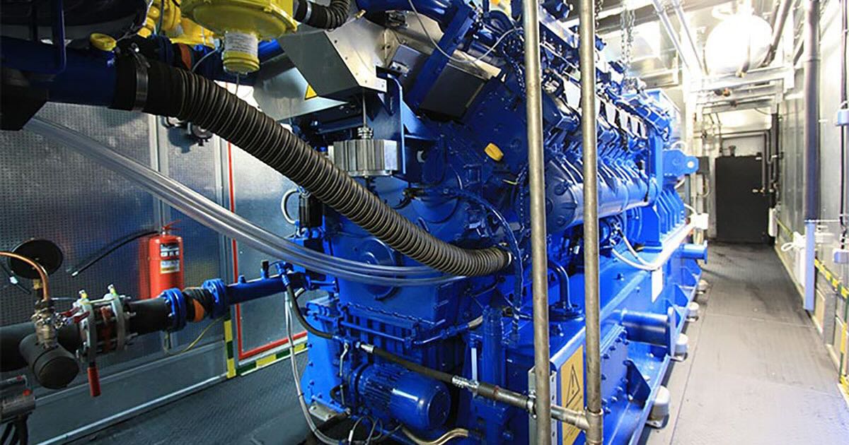 Interior view of a container CHP plant at a logistics center in Yaroslavl, Russia, featuring a single MWM TCG 2020 V12 engine in Signature Blue. The well-lit container shows industrial structures like pipes, and there is space to walk along the right side of the engine. The plant operates round-the-clock for maximum energy security.