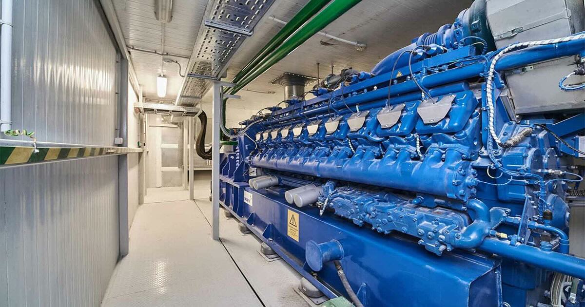 MWM TCG 2020 V20 gas engine in signature blue inside a containerized CHP plant, with a narrow walkway running alongside the genset and the MWM logo visible at the far end.