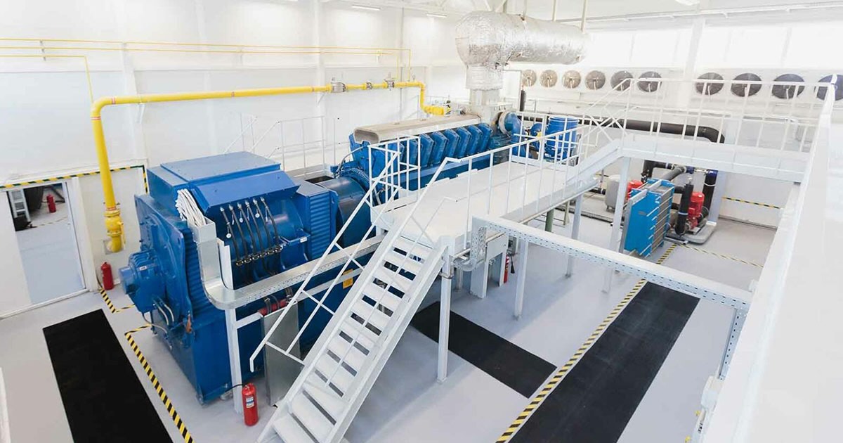 MWM TCG 2032B V16 engine in Signature Blue inside a bright hall at NLMK Ural CHP plant, producer of billets and long steel products. A bright metal staircase with platform provides access to the upper parts of the engine.