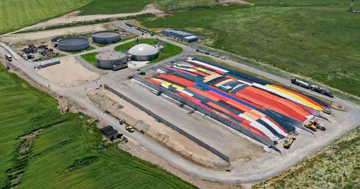 Bird’s-eye view of the Saramzalino biogas plant in North Macedonia with two MWM TCG 2020 V12 engines. The site is surrounded by green meadows and fields, with biogas structures, colorful field sections, industrial vehicles, a building, and a road encircling the facility.
